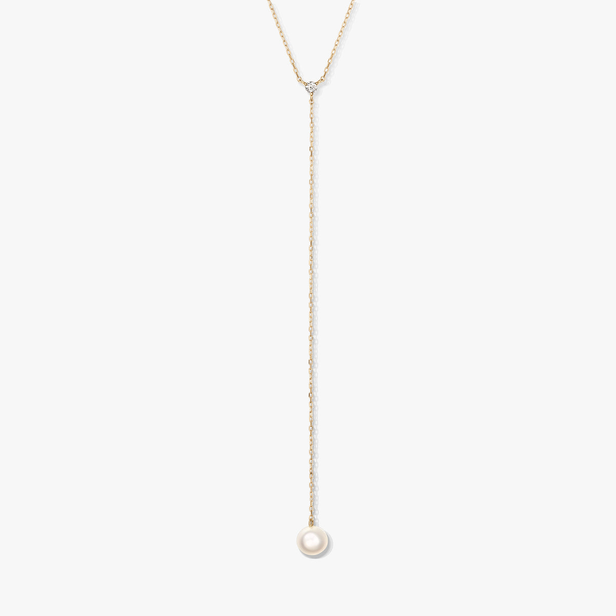Minimalista arany lariat nyaklánc egyetlen kerek fehér gyöngyfüggővel és apró díszkővel, fehér háttéren középre helyezve.
