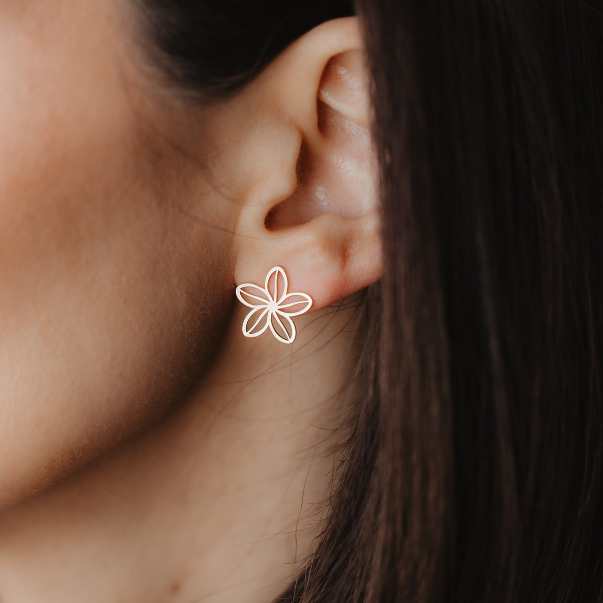 Közelkép egy fülről, amelyen egy finom, 14K sárga arany, áttört, virág alakú bedugós fülbevaló látható.